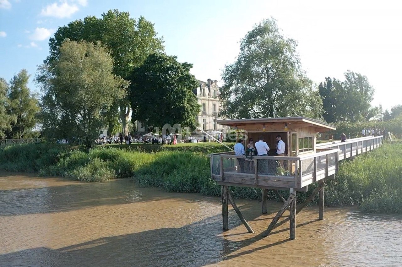 Un ponton en bois surplombant une rivière, entouré de verdure et d'arbres, avec des personnes rassemblées dessus.