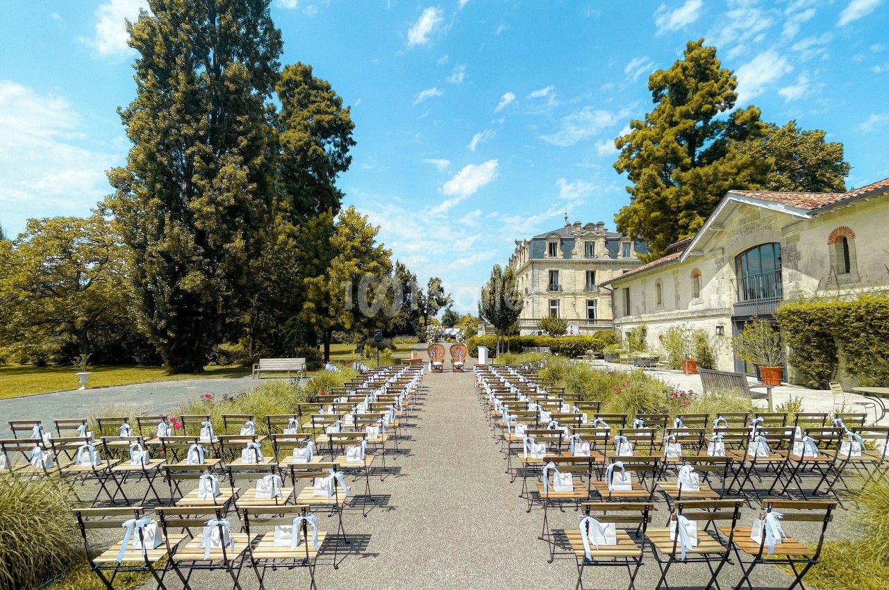 Chaises alignées en extérieur pour une cérémonie, avec un bâtiment ancien et des arbres en arrière-plan.