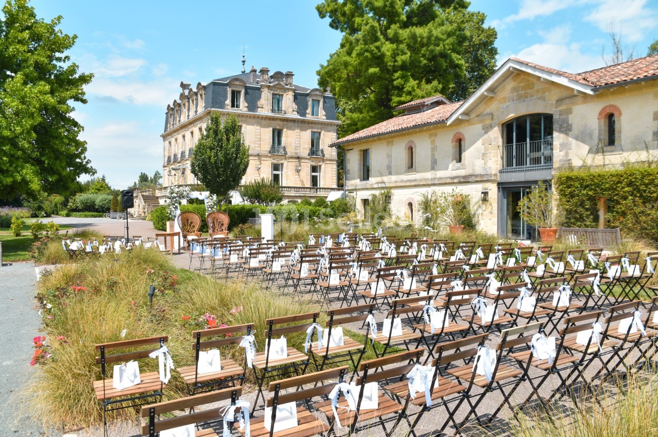 Chaises alignées en extérieur pour un événement, devant un bâtiment historique entouré de verdure.