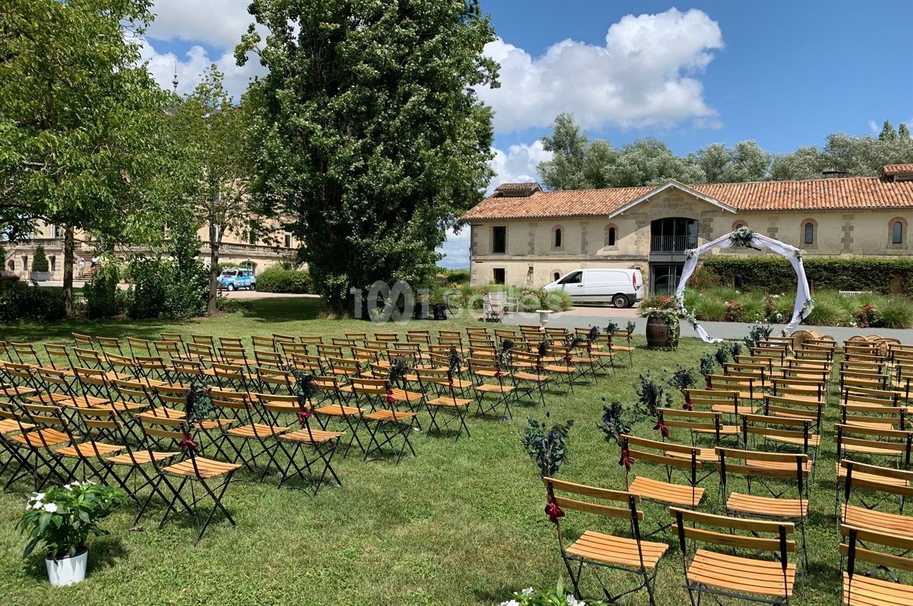 Chaises en bois disposées en rangées sur une pelouse pour une cérémonie en plein air, avec un arche décoré en arrière-plan.