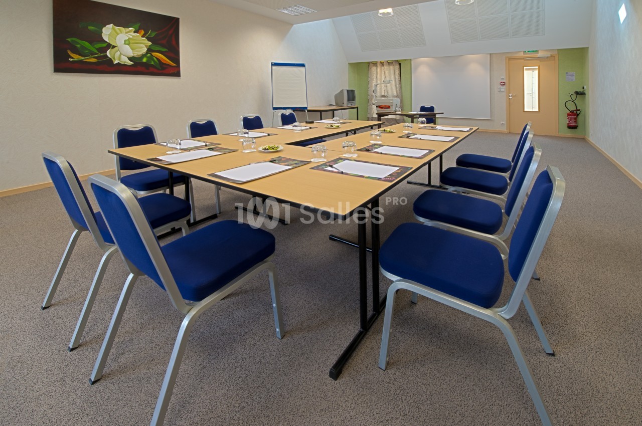 Salle de réunion avec une grande table rectangulaire, des chaises bleues, un tableau de conférence et un tableau mural.