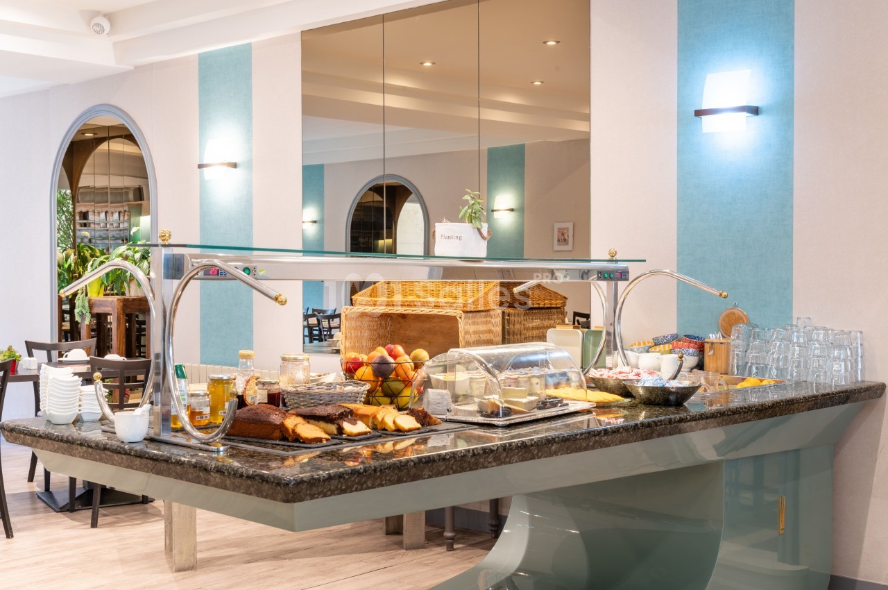 Buffet de petit-déjeuner avec viennoiseries, fruits, céréales et boissons, présenté dans une salle lumineuse.