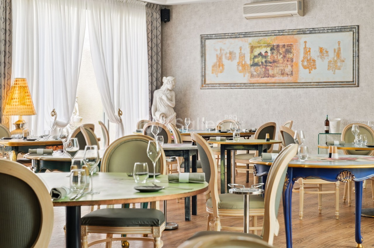Salle de restaurant élégante avec tables dressées, chaises classiques, lumière naturelle et décoration artistique.