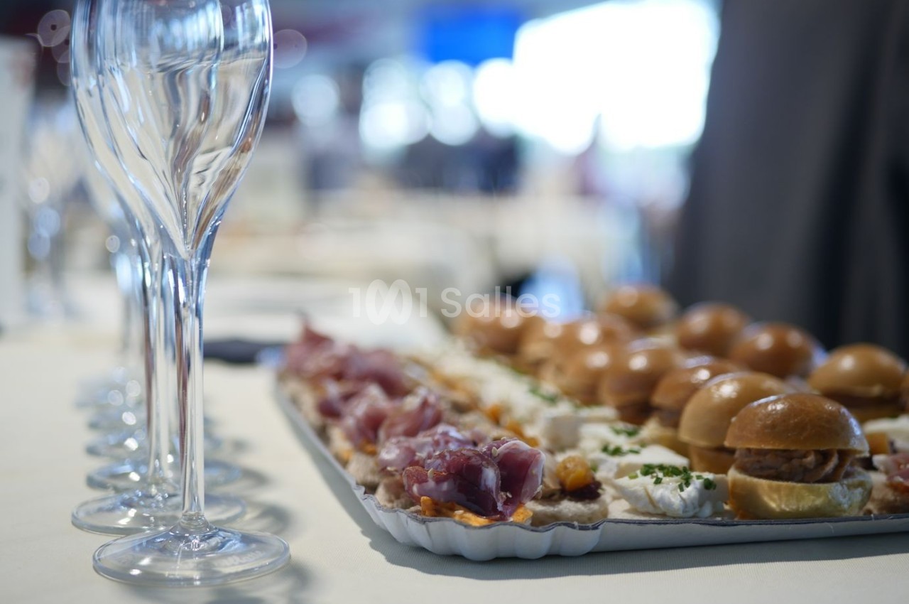 Plateau de bouchées apéritives avec charcuterie et mini-burgers, posé sur une table près de flûtes en verre.