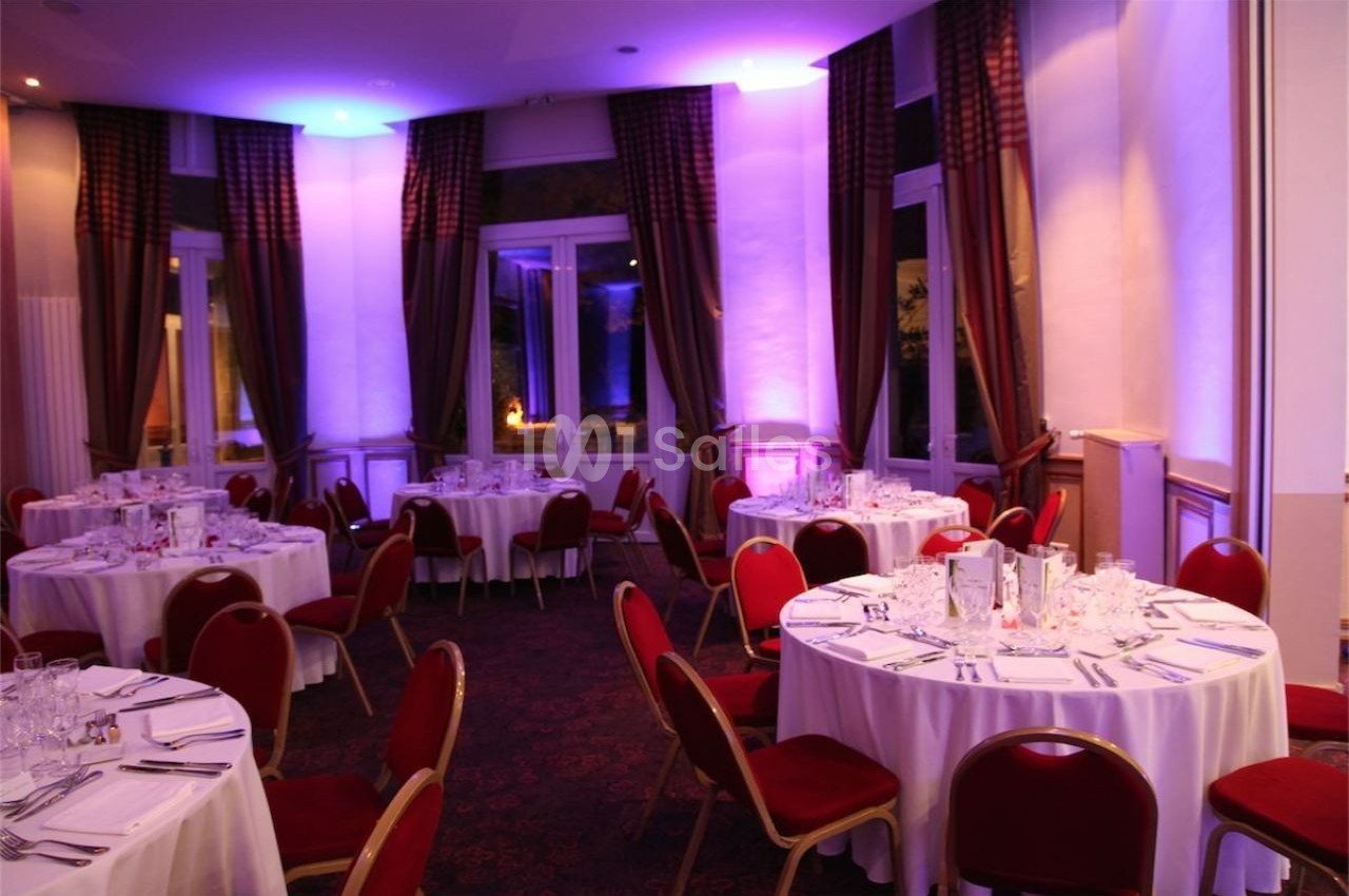 Salle de réception élégante avec tables rondes dressées, nappes blanches et éclairage tamisé violet.