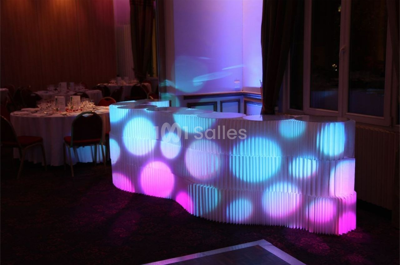Comptoir lumineux blanc avec motifs circulaires colorés dans une salle de réception sombre.