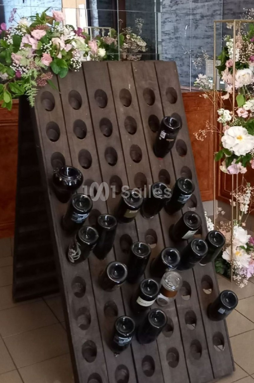 Support en bois incliné avec des bouteilles en verre insérées, entouré de décorations florales.