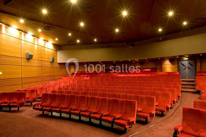 Salle de cinéma vide avec des rangées de fauteuils rouges et un éclairage tamisé au plafond.