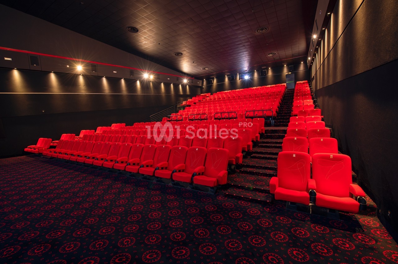 Salle de cinéma vide avec des rangées de sièges rouges et un sol recouvert de moquette à motifs.