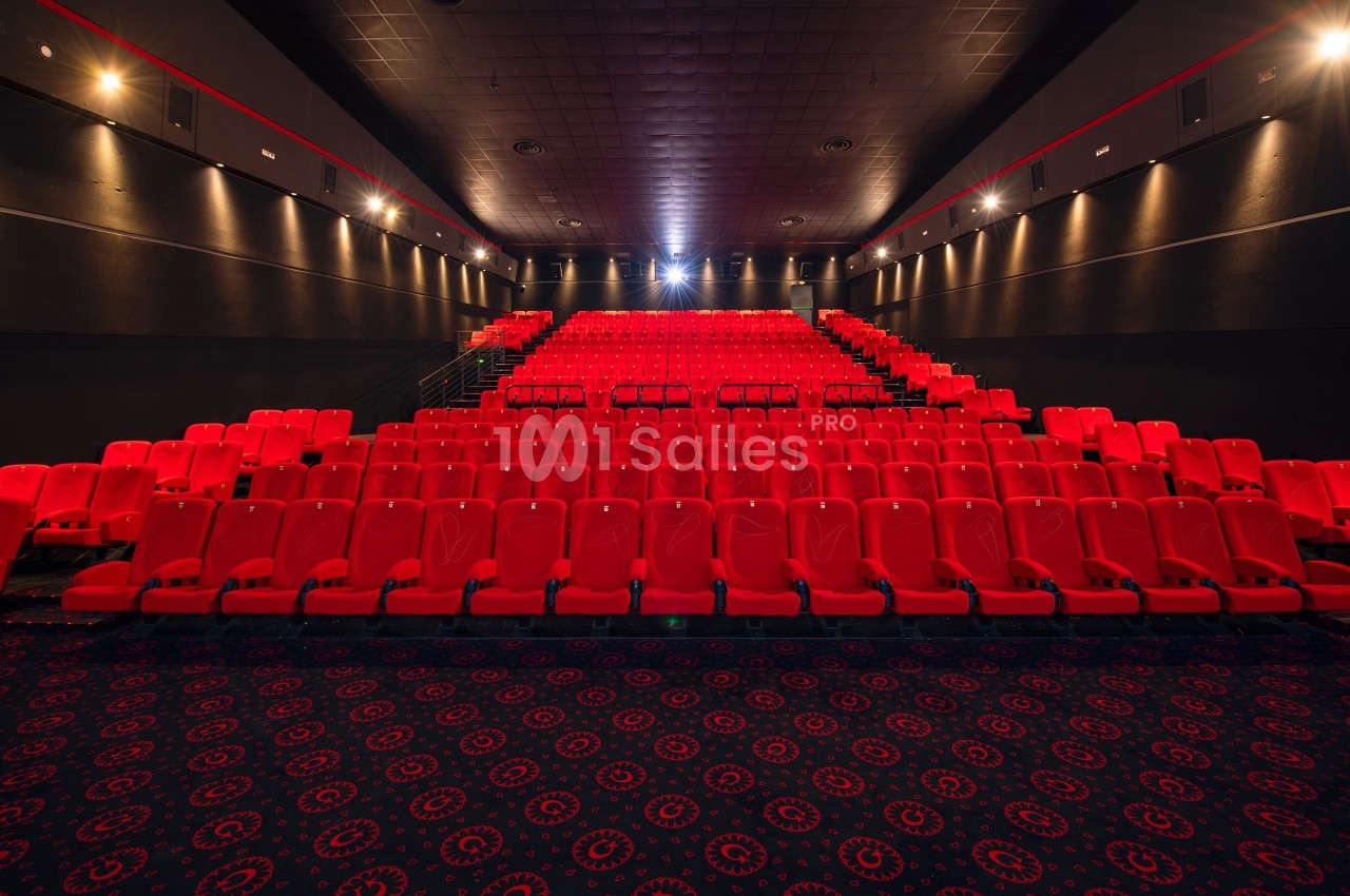 Salle de cinéma vide avec des rangées de sièges rouges et un éclairage tamisé.