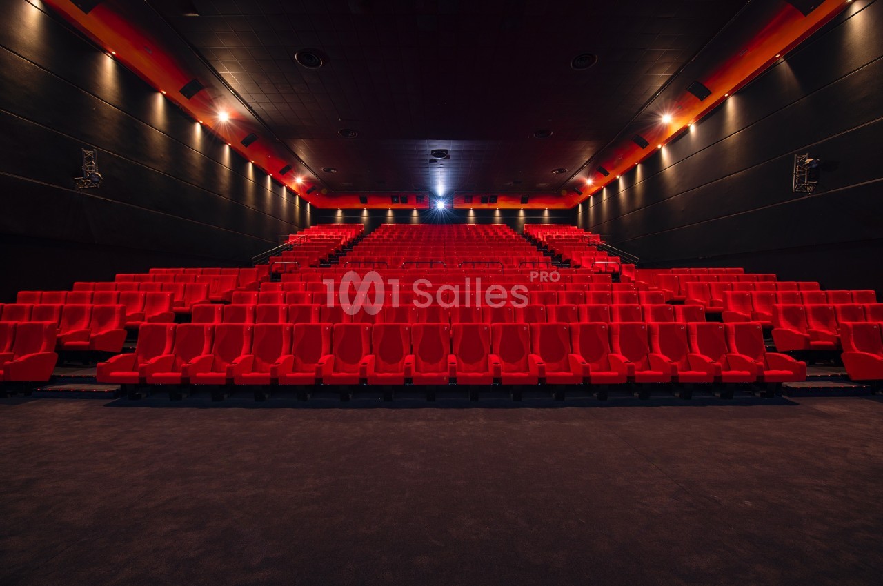 Salle de cinéma vide avec des rangées de sièges rouges et un écran éteint au fond.