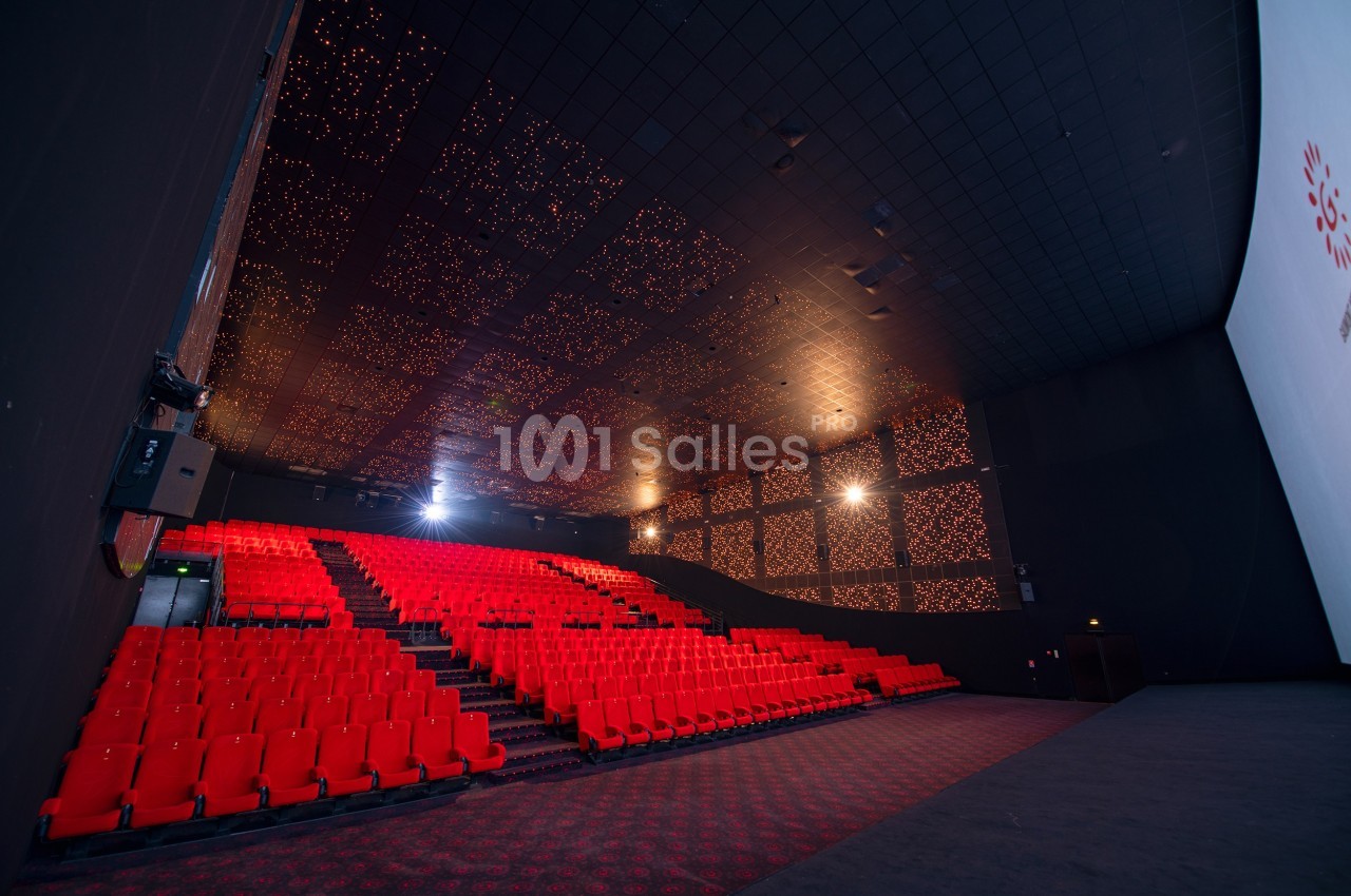 Salle de cinéma vide avec sièges rouges, écran blanc et plafond décoré de lumières.