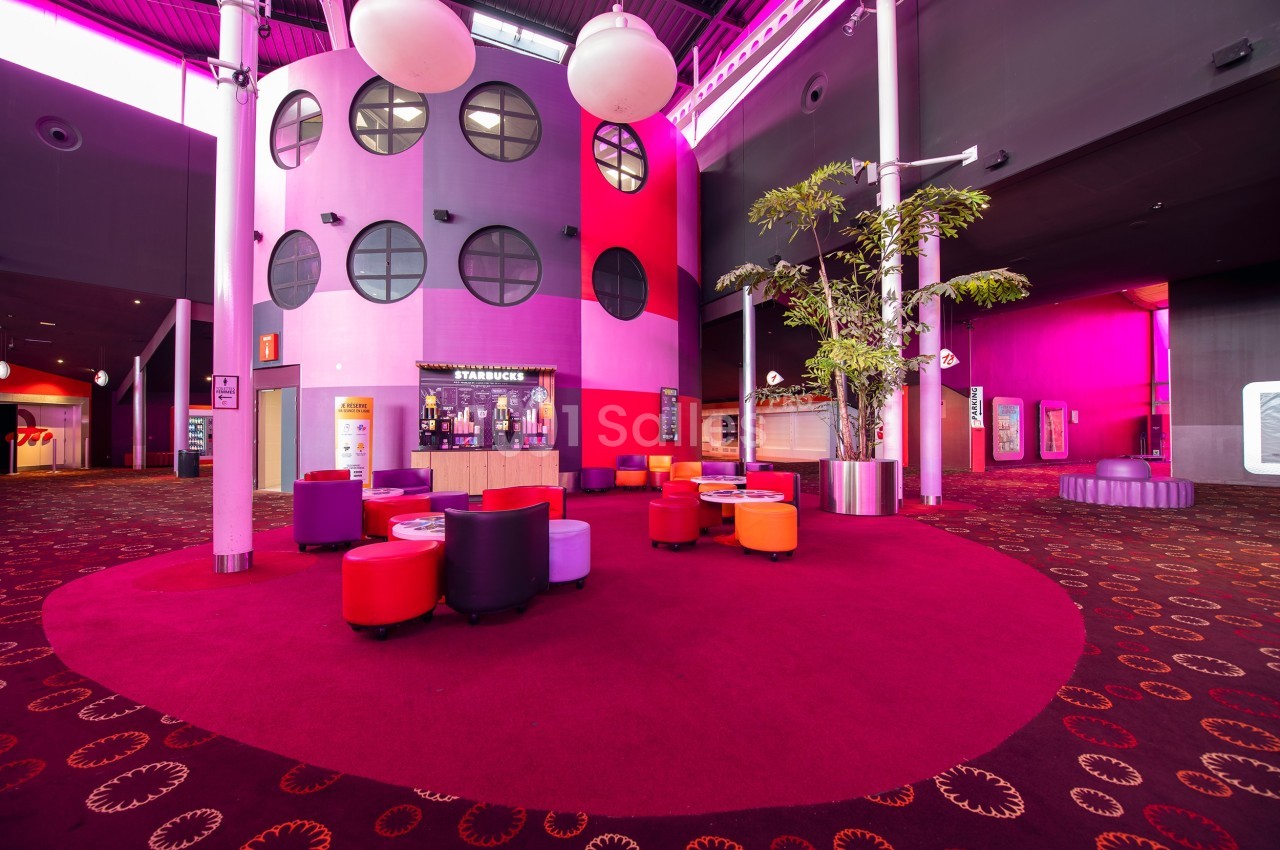 Espace intérieur coloré avec fauteuils rouges et violets, sol moquetté et décorations lumineuses modernes.