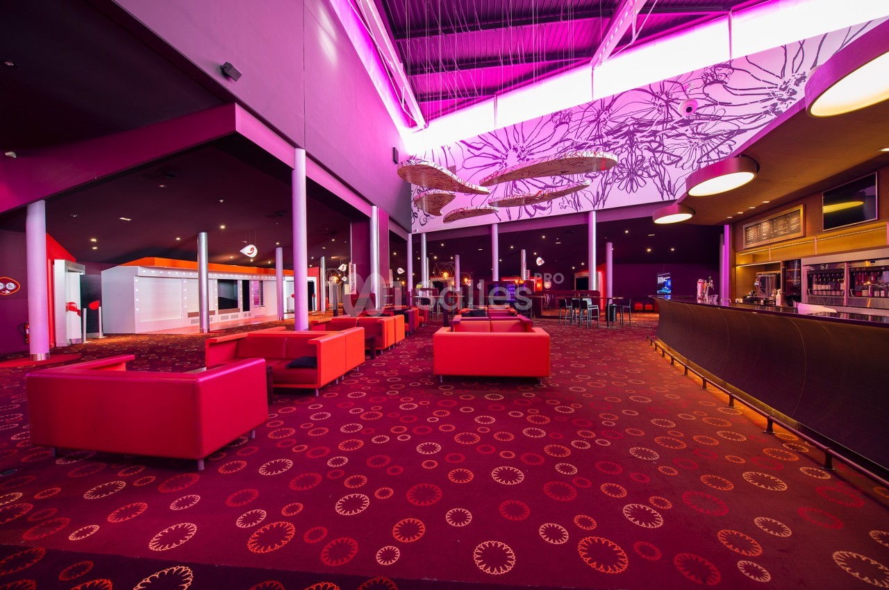 Intérieur d'un espace lounge avec fauteuils rouges, bar à droite et éclairage néon rose au plafond.