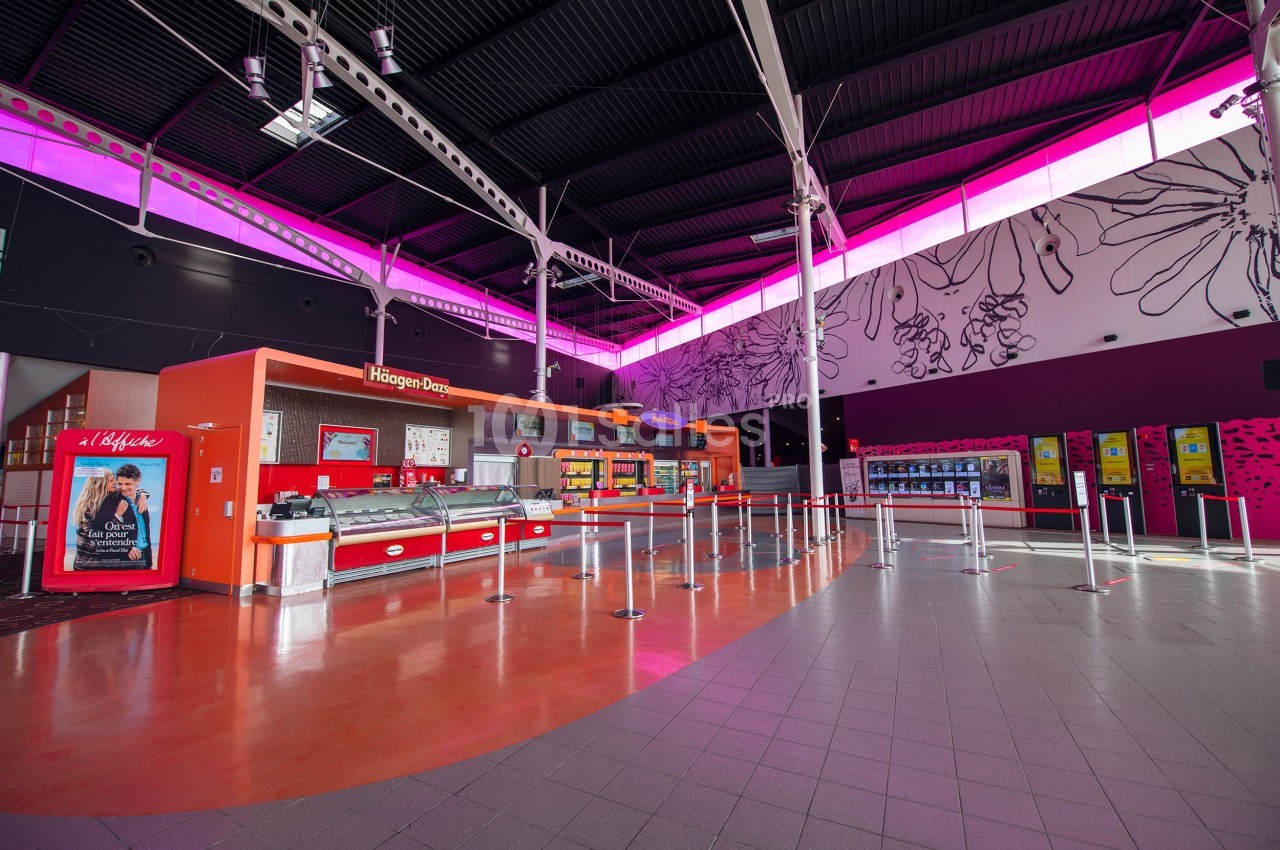 Comptoir de glaces et snacks dans un espace lumineux avec décorations murales et éclairage rose au plafond.