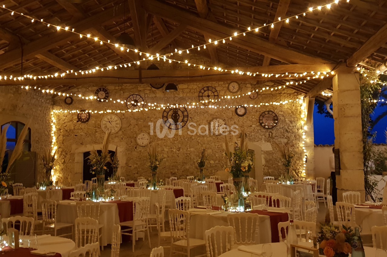 Salle en pierre décorée de guirlandes lumineuses, tables dressées avec nappes rouges et arrangements floraux.