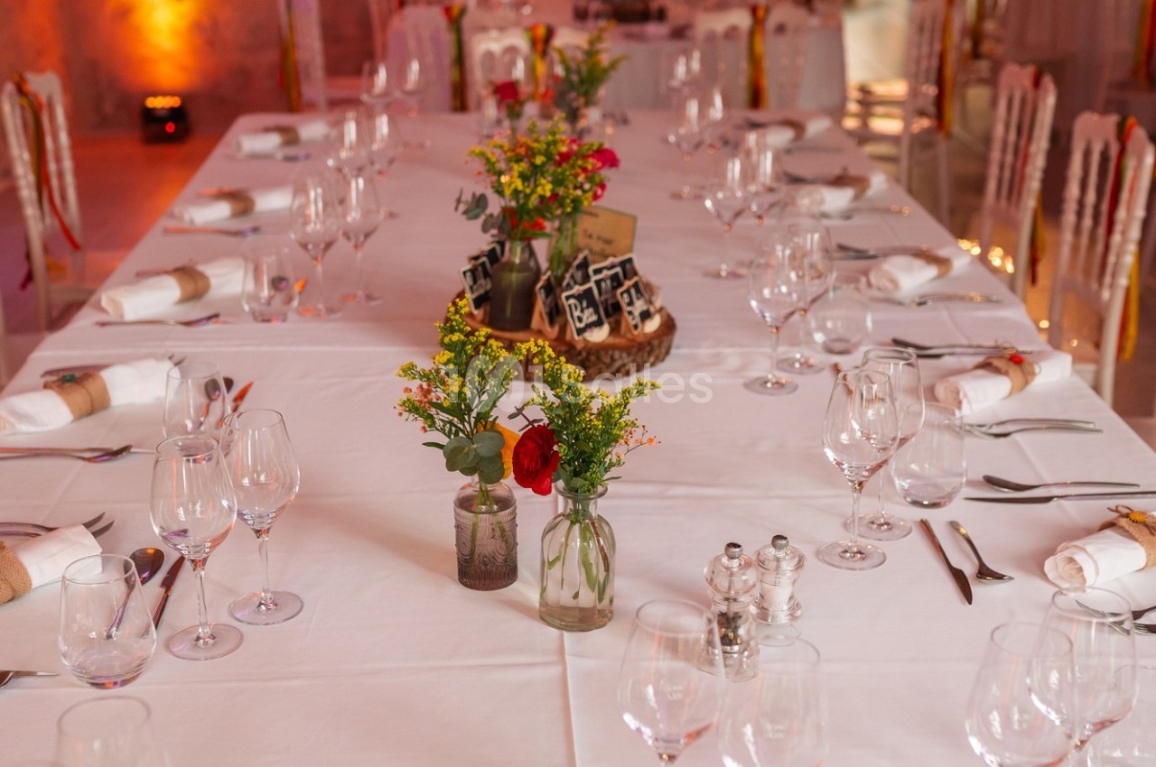 Grande table dressée avec nappes blanches, vaisselle élégante et décorations florales au centre.