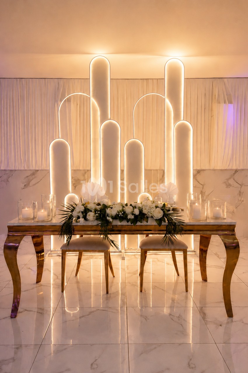 Table décorée avec des fleurs blanches et bougies, devant un fond lumineux avec des arches modernes.
