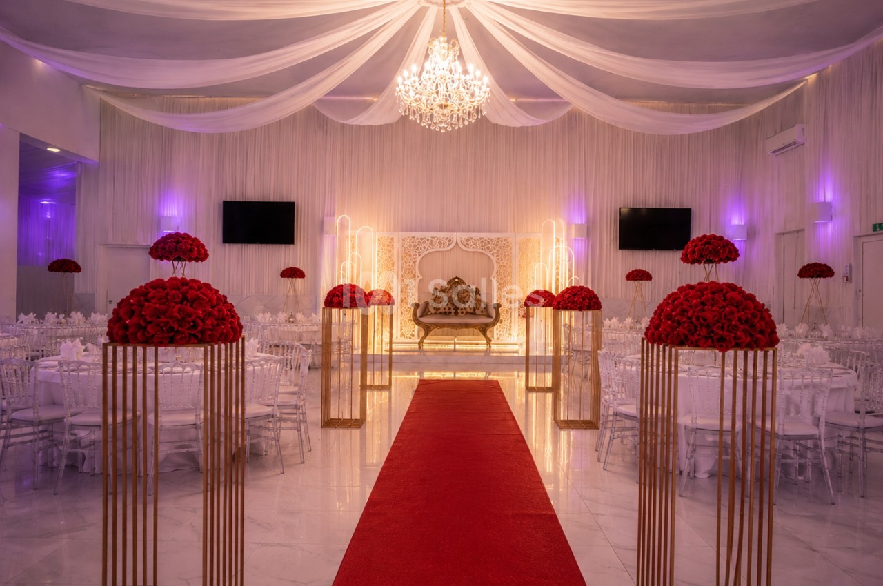 Salle de réception décorée avec un tapis rouge, des bouquets de roses rouges et un canapé doré sous un lustre.