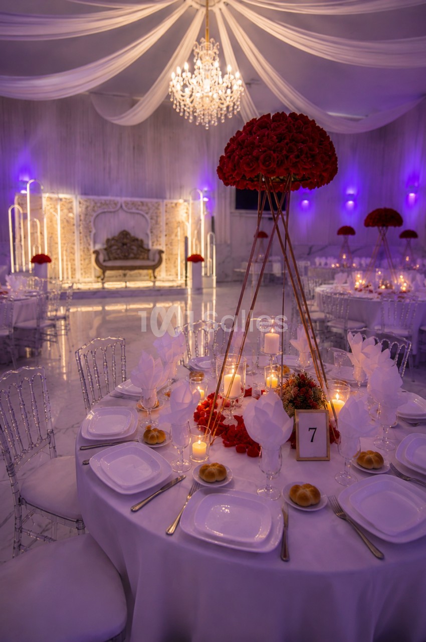 Salle de réception élégante avec tables décorées, centre de table floral rouge et éclairage tamisé.