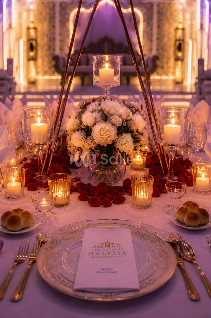 Table élégamment dressée avec des bougies, un bouquet de fleurs blanches et des pétales rouges, dans une ambiance festive.