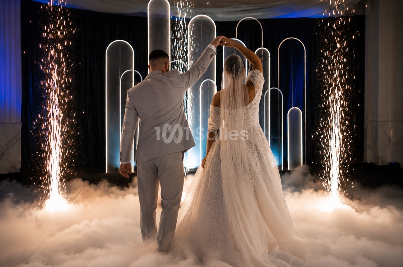 Un couple danse au milieu de fumée et d'étincelles, entouré d'arcs lumineux dans une ambiance festive.