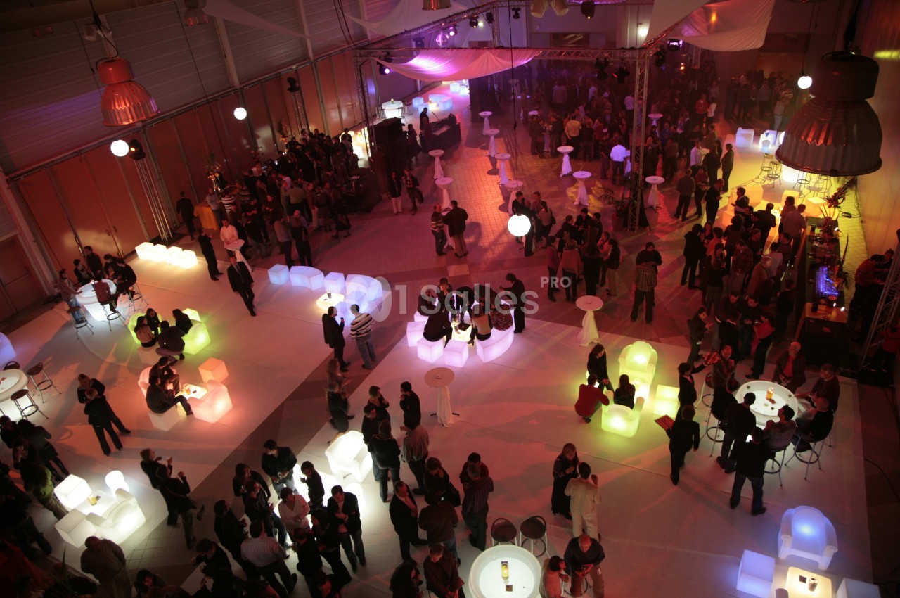 Salle événementielle animée avec des groupes de personnes autour de tables lumineuses et un éclairage tamisé.
