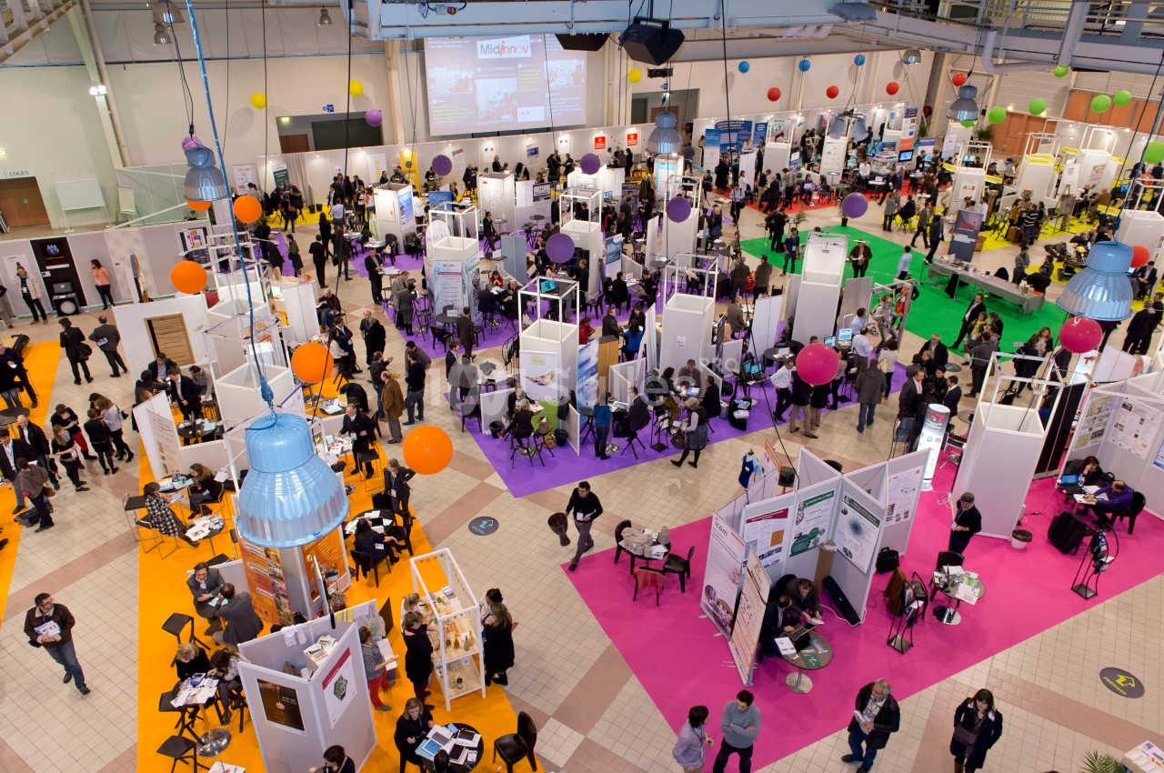 Vue aérienne d'un salon professionnel avec des stands colorés, des visiteurs et des animations dans un grand espace…