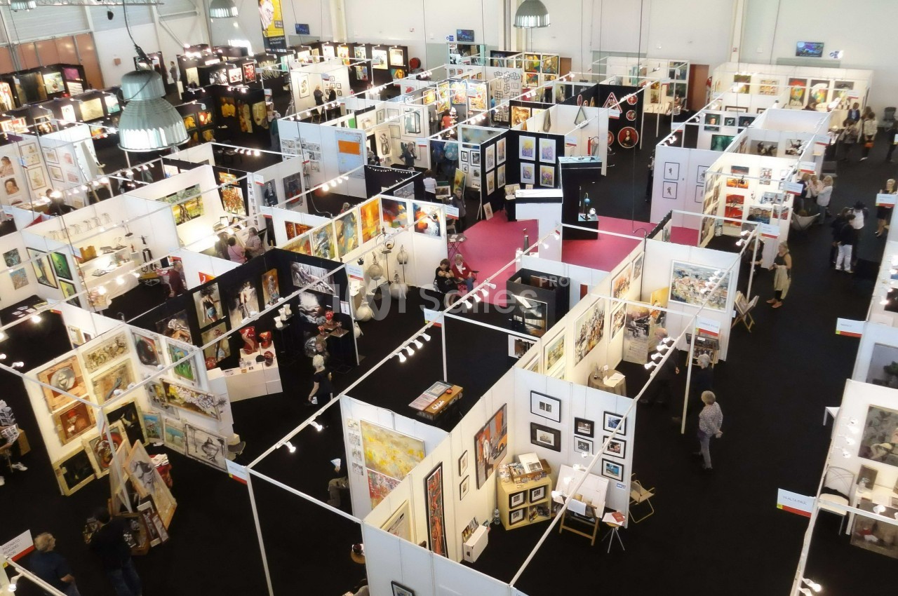 Vue aérienne d'une exposition artistique avec des stands présentant des œuvres variées et des visiteurs circulant.
