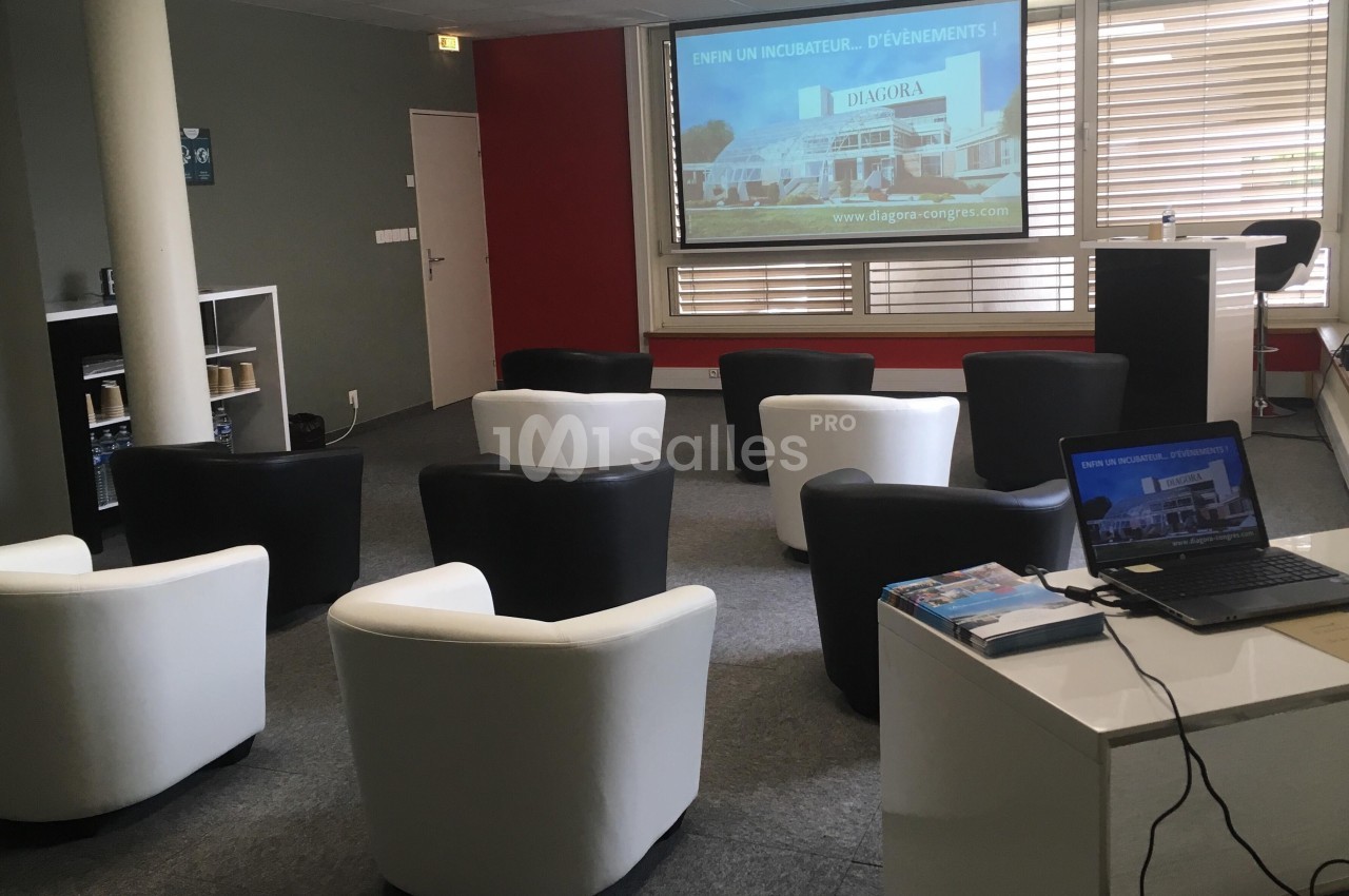 Salle de réunion avec fauteuils disposés face à un écran de projection et un ordinateur portable sur un bureau.