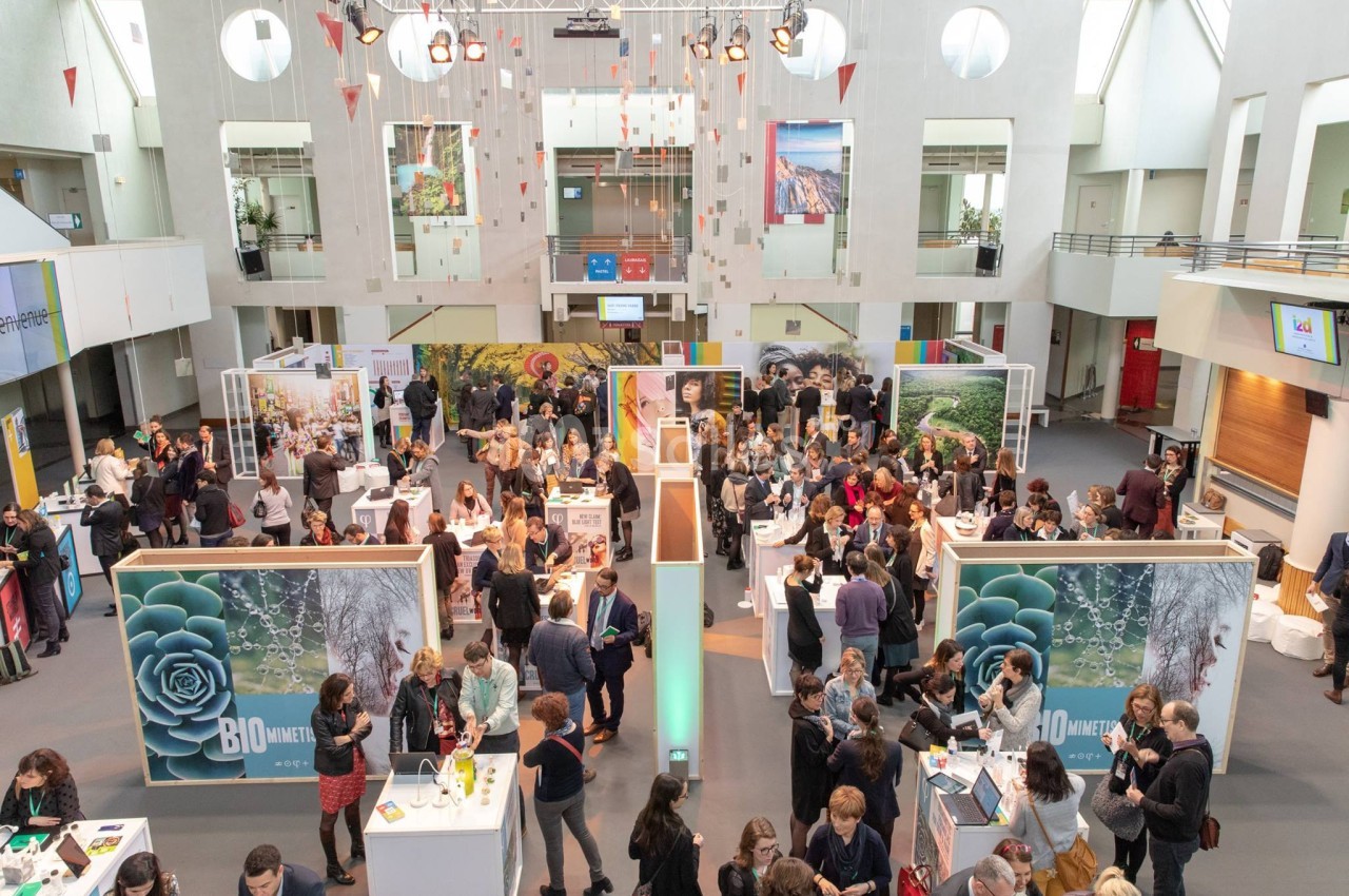 Vue d'un salon professionnel avec des stands, des visiteurs échangeant et un décor lumineux dans un grand espace intérieur.