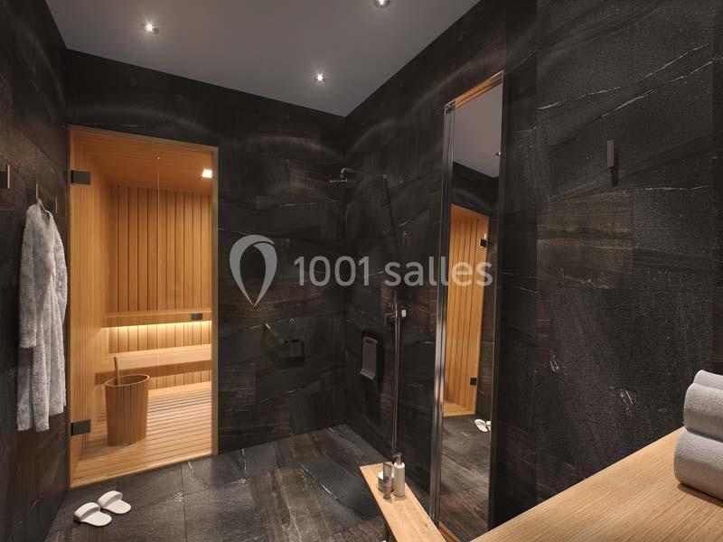 Salle de bain moderne avec murs sombres, douche à l'italienne et vue sur un sauna en bois éclairé.