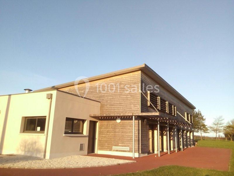 Bâtiment moderne avec façade en bois et toit incliné, entouré d'un espace extérieur dégagé.