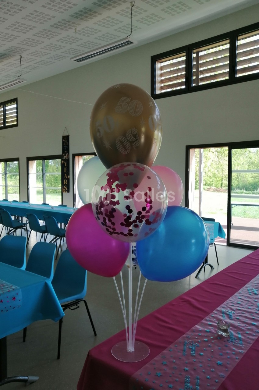 Bouquet de ballons colorés décorant une salle avec des tables dressées et une vue sur l'extérieur.