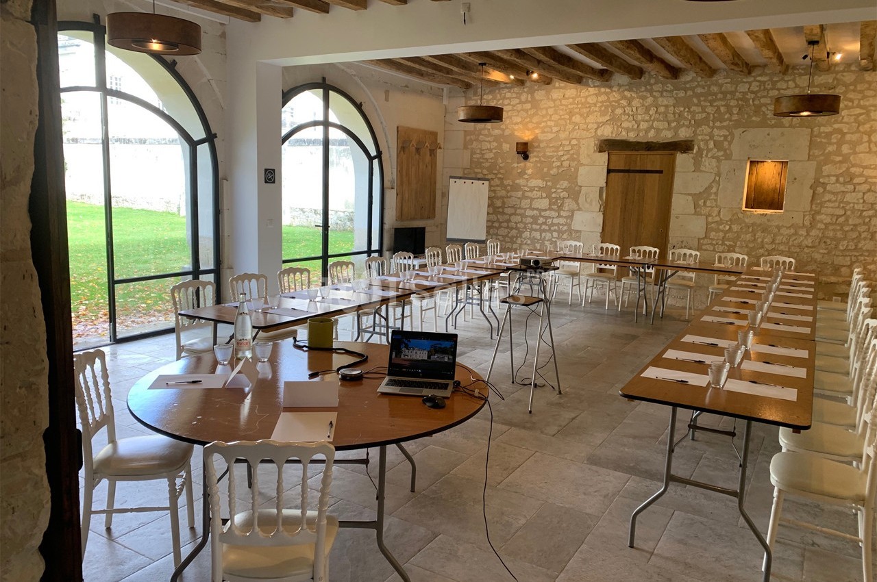 Salle de réunion lumineuse avec tables, chaises blanches et matériel de présentation, donnant sur un jardin verdoyant.