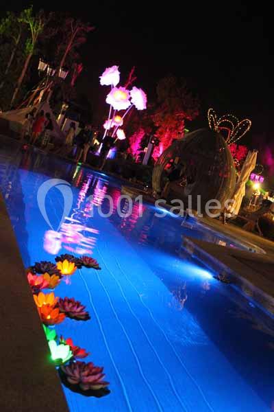 Piscine éclairée la nuit avec des fleurs lumineuses flottantes et des décorations colorées en arrière-plan.