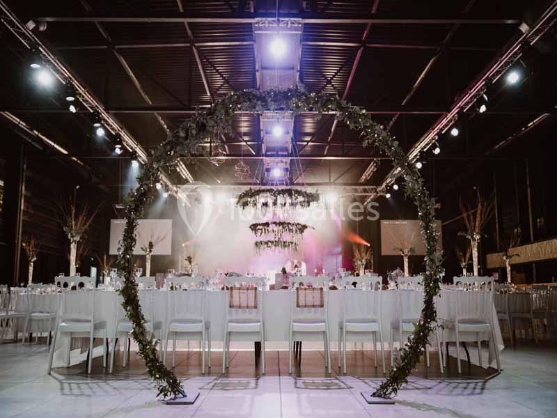 Salle de réception décorée avec des tables dressées et un grand cercle végétal au premier plan sous un éclairage tamisé.