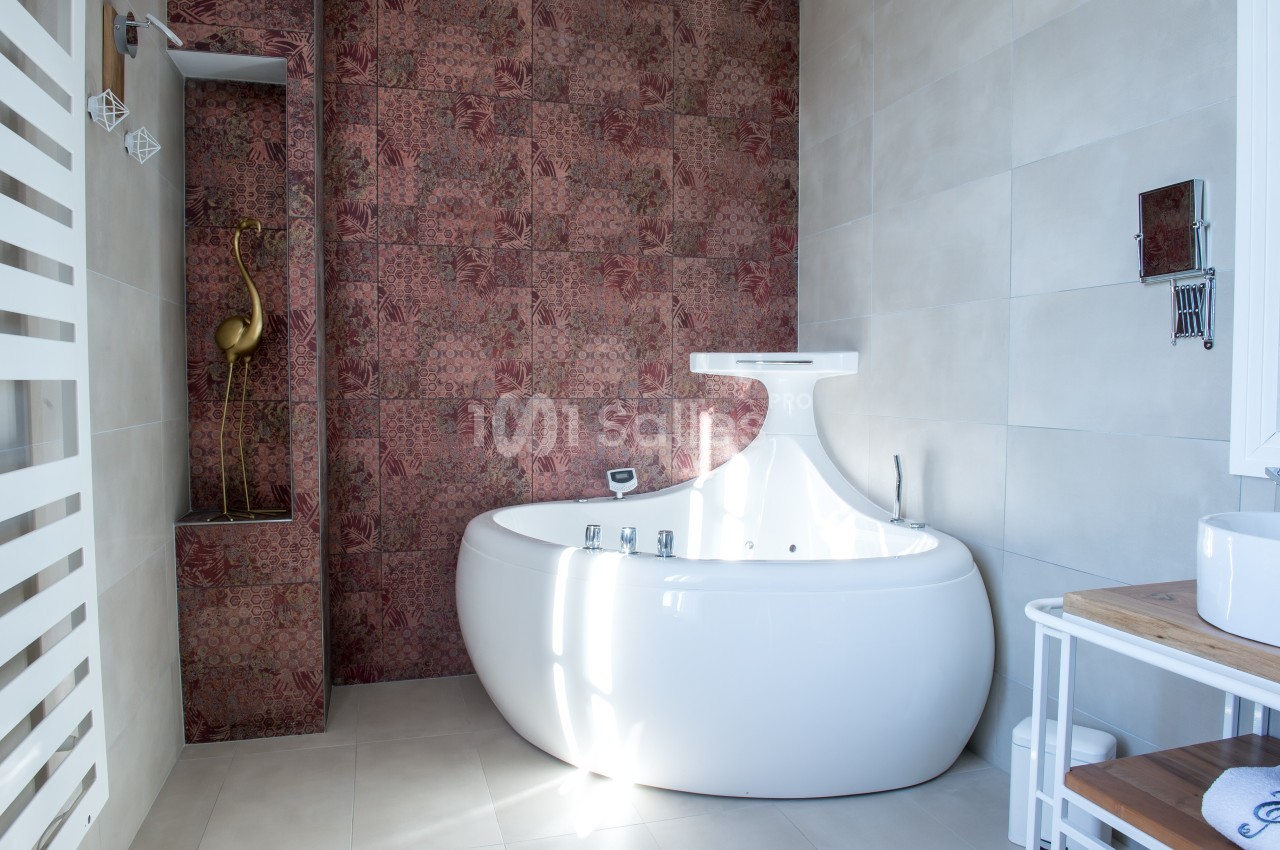 Salle de bain avec baignoire blanche moderne, mur en mosaïque rouge et étagère décorative avec une sculpture dorée.