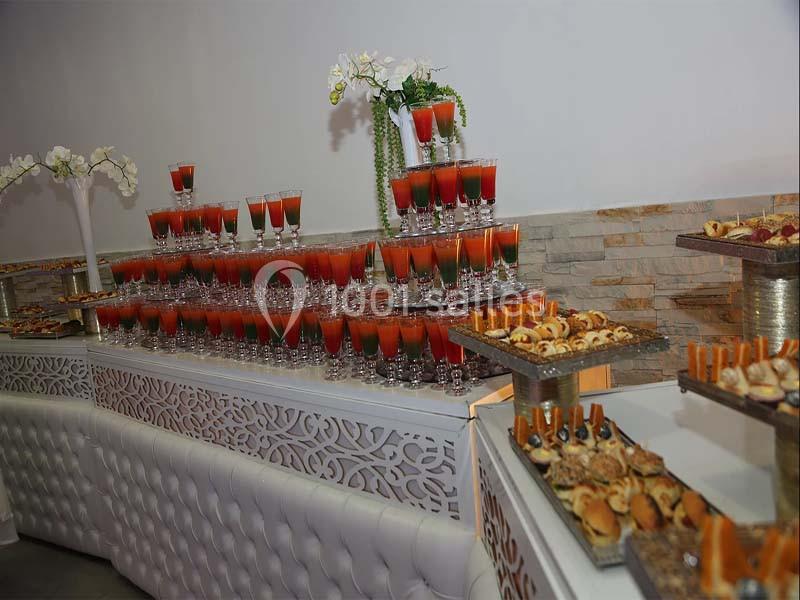 Buffet avec verrines colorées, fleurs blanches en décoration et assortiments de petits fours sur des plateaux.