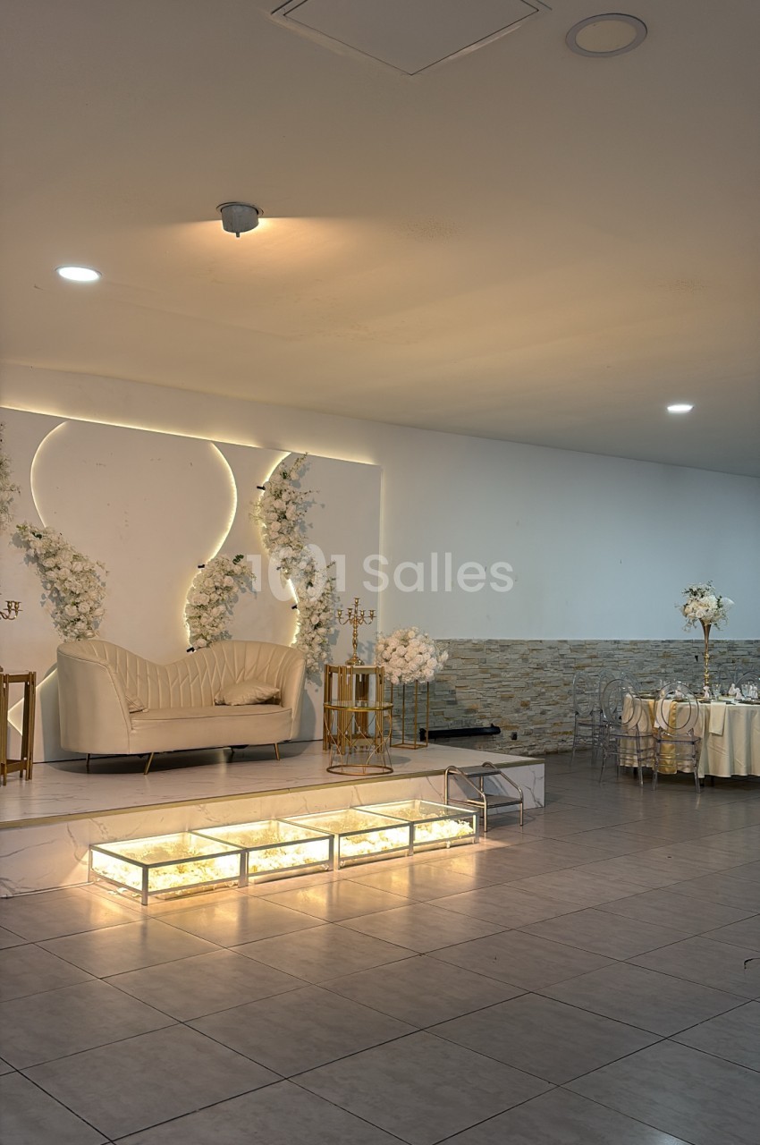Salle intérieure aux murs clairs, canapé blanc crème face à un décor floral blanc et or, allée centrale illuminée.