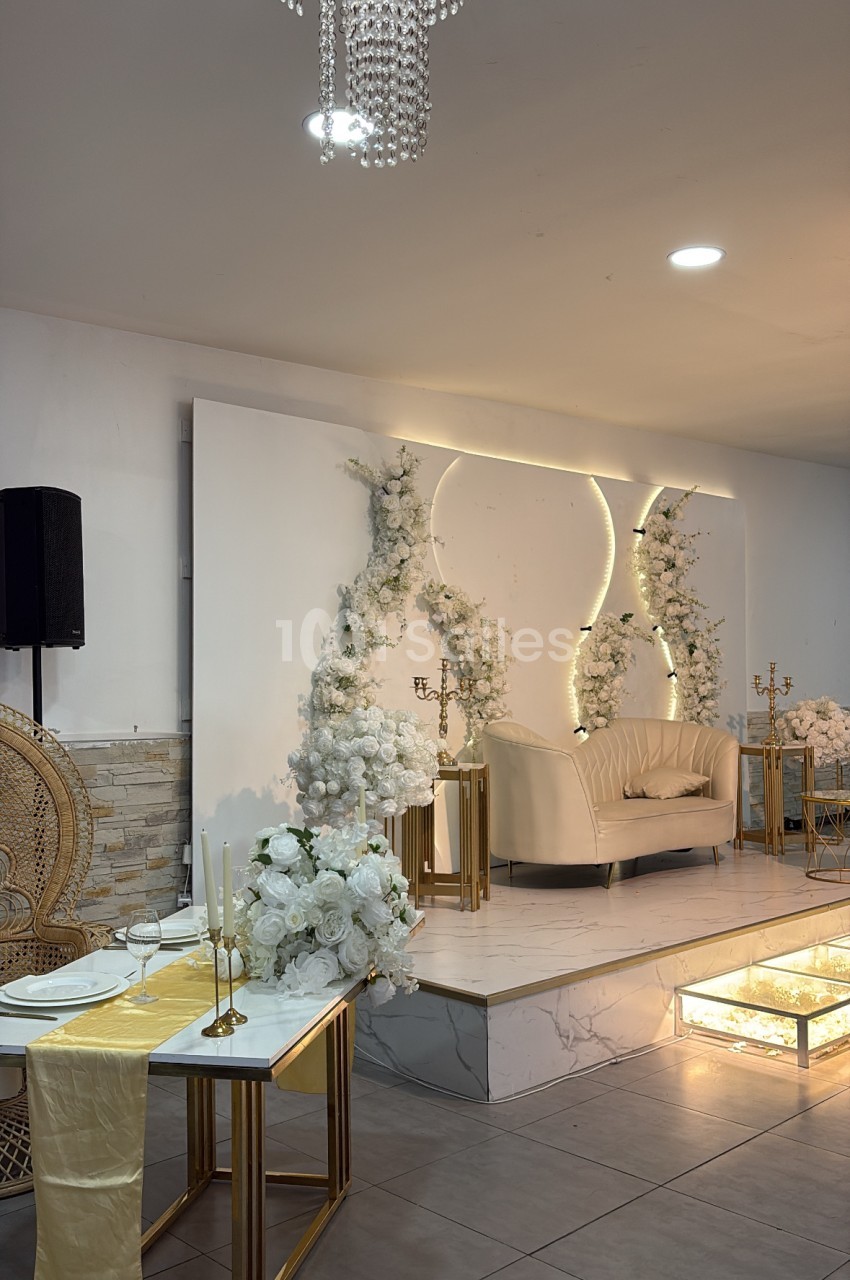 Salle dressée avec table en marbre, chaise beige, murs blancs et néons, fleurs blanches, lustre cristal et éclairage tamisé.