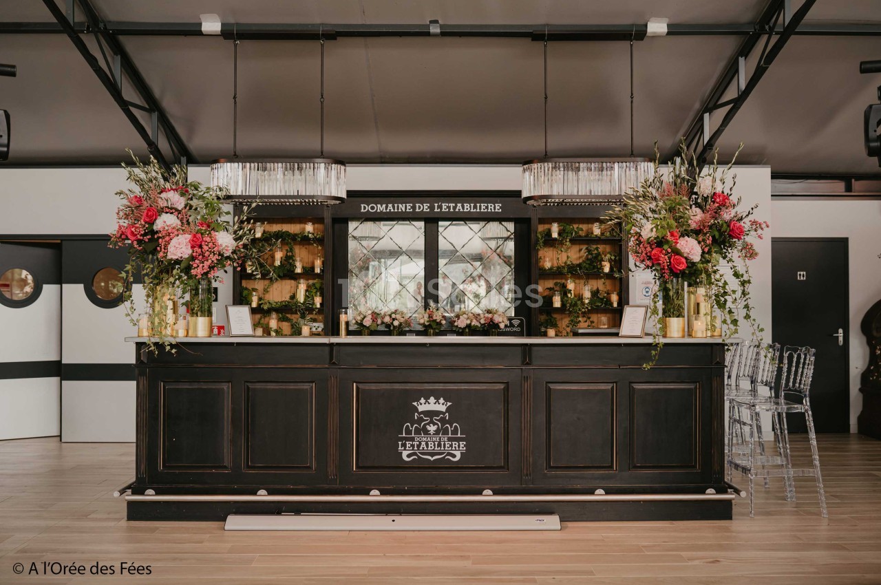 Comptoir en bois sombre décoré de fleurs colorées, situé dans une salle lumineuse avec des éléments modernes et élégants.