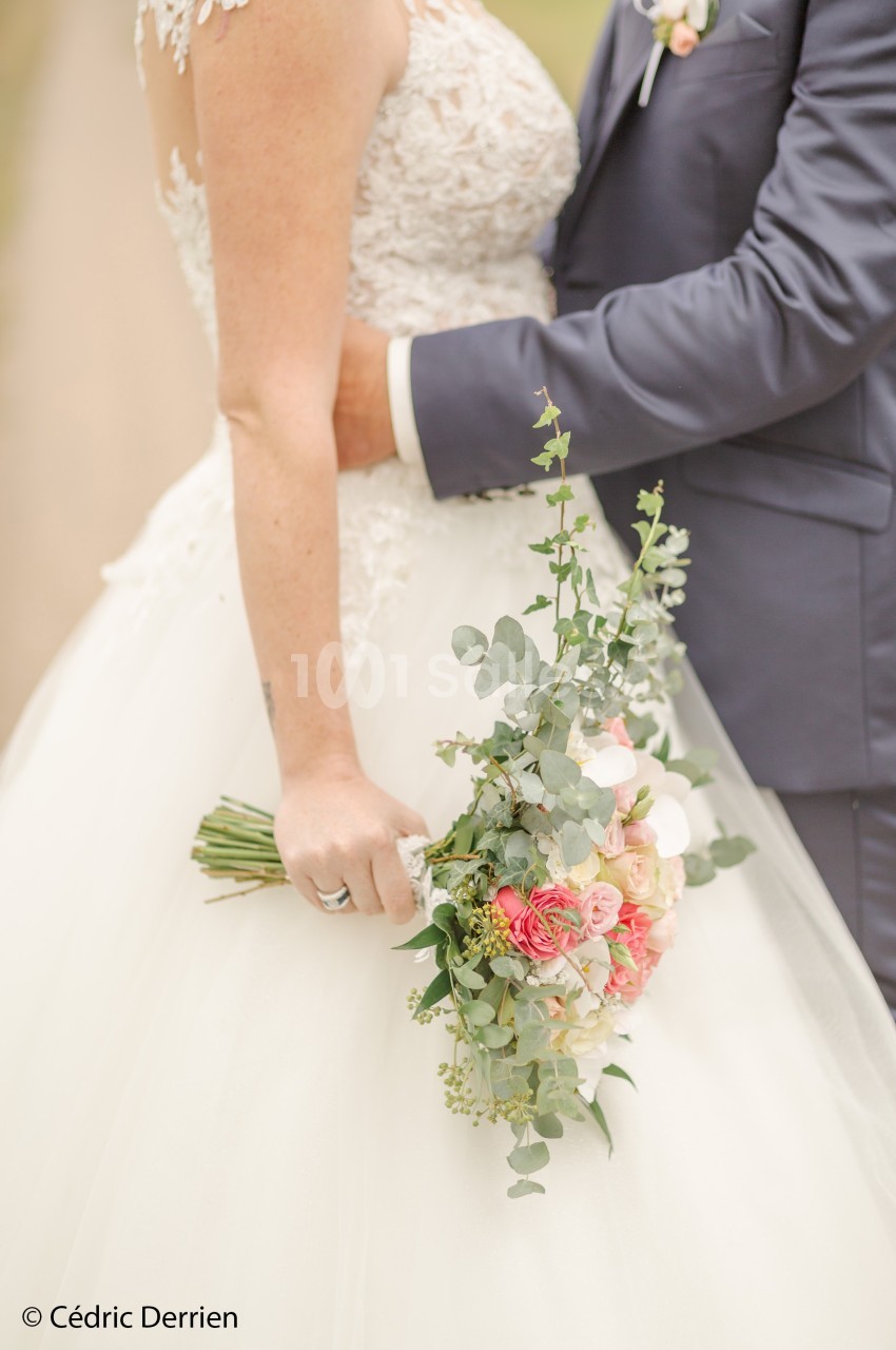 Un couple de mariés en tenue de cérémonie, tenant un bouquet de fleurs pastel avec des touches de vert.