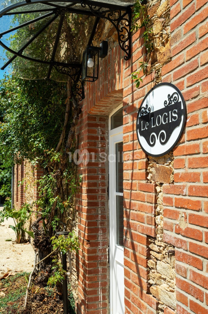 Façade en briques avec une porte blanche, une enseigne ’Le Logis’ et un auvent en fer forgé.