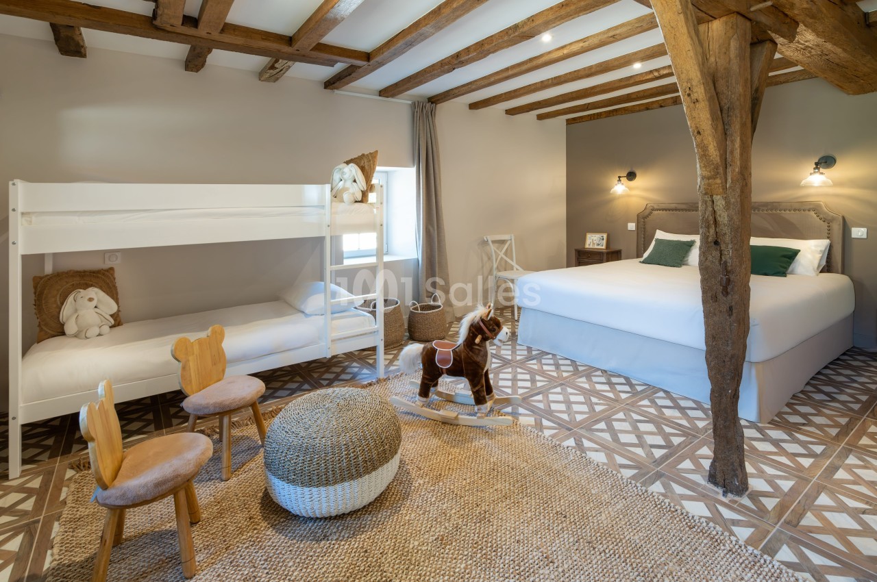 Chambre lumineuse avec lits superposés, lit double, poutres apparentes, jouets en bois et décoration chaleureuse.