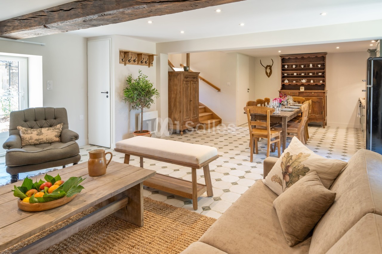 Salon lumineux avec mobilier en bois, table à manger, canapé beige, et décoration rustique dans un intérieur spacieux.