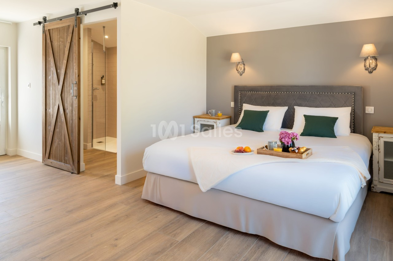 Chambre lumineuse avec lit double, tête de lit capitonnée, tables de chevet, porte coulissante en bois et salle de bain…