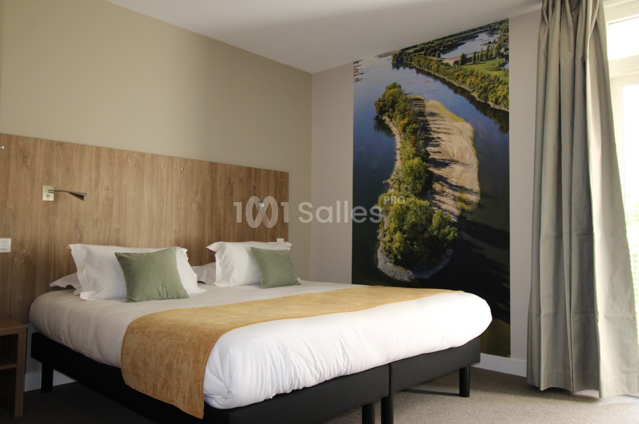 Chambre d'hôtel avec lit double, tête de lit en bois, décor mural représentant une rivière et lumière naturelle.
