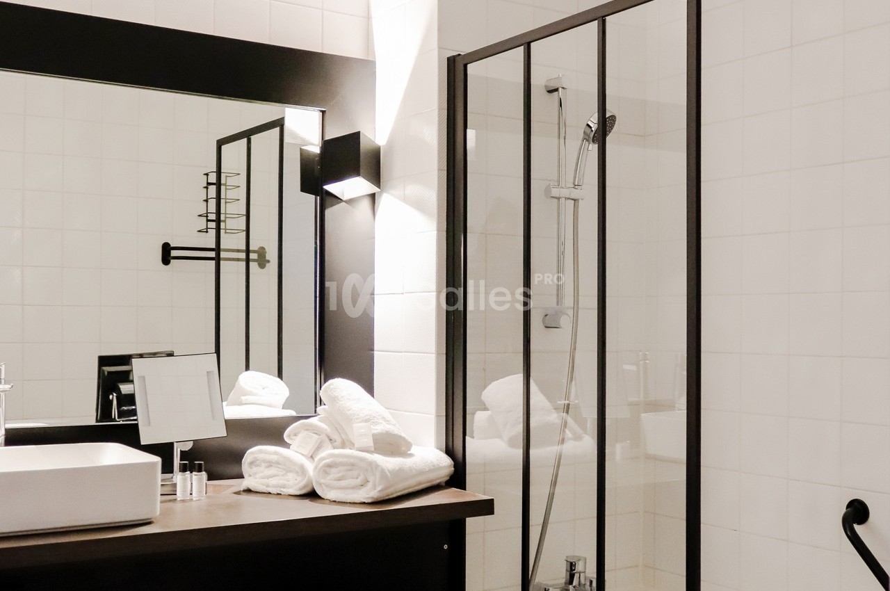 Salle de bain moderne avec douche vitrée, lavabo rectangulaire, miroir éclairé et serviettes pliées sur le comptoir.