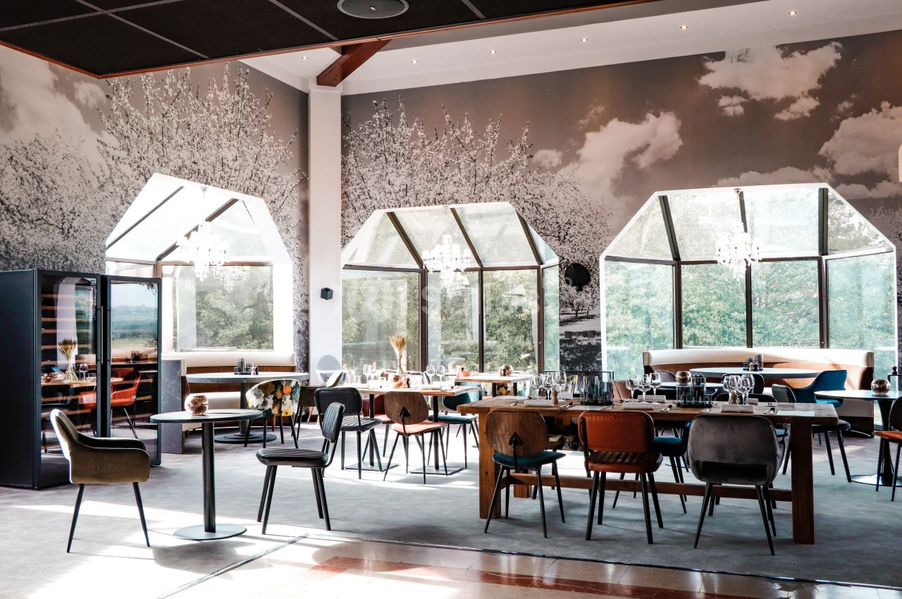 Salle de restaurant lumineuse avec de grandes baies vitrées, des tables dressées et un décor mural en noir et blanc.